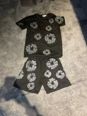 Svart och grått sett  - Säljer ett par svarta shorts och tröja  med stora gråa cirkelmönster. Shortsen har loose passform och elastisk midja, vilket gör dem riktigt bekväma. Materialet känns som bomull och är perfekt för sommaren. Grymt coola för dig som gillar att sticka ut.
