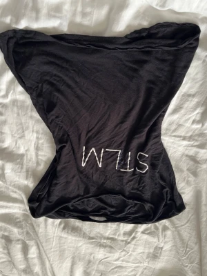 Svart t-shirt från Ellos med text - Säljer en T-shirt från Ellos med vit text 'SLIM' framtill. Toppen har en tight passform, perfekt för att styla med jeans eller kjol. Materialet känns mjukt och stretchigt, vilket gör den bekväm att bära.