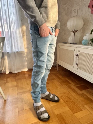 Replay ANBASS - Säljer ett par ljusblå slim fit jeans med klassisk femficksdesign och normal midja. Jeansen har en snygg tvättad look och smala ben som sitter tajt hela vägen ner. Perfekta till en avslappnad streetwear-stil.