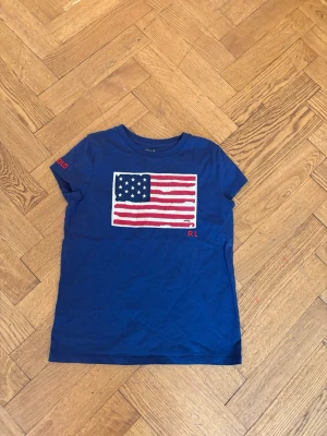  Ralph Lauren t-shirt  - Snygg blå t-shirt från Ralph Lauren med amerikansk flagga tryckt på bröstet och RL-brodyr.
