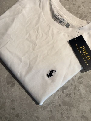 Vit t-shirt från Polo Ralph Lauren - Kan prutas. Säljer tröjan eftersom att den inte får plats i garderoben. t-shirt från Polo Ralph Lauren med ikonisk broderad logga på bröstet. Tröjan är tillverkad i bomull. Perfekt att använda som en chill T-shirt.