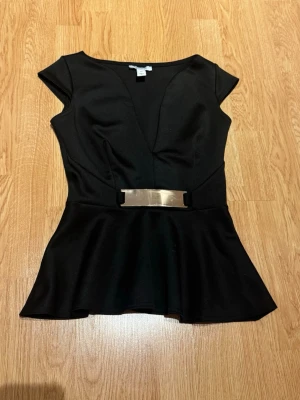 Svart peplum topp med metallbälte - Snygg svart peplum topp med djup v-ringning och korta ärmar. Aldrig använt den då den är för liten för mig!💕