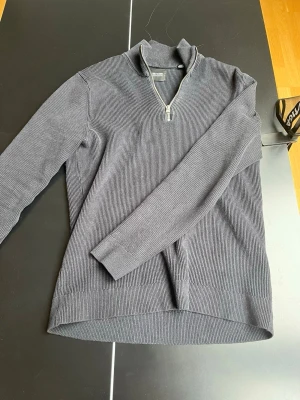 Mörkgrå stickad tröja Only & Sons - Snygg mörkgrå stickad tröja från Only & Sons med halv dragkedja och hög krage. Tröjan har ribbad struktur och långa ärmar, perfekt för lager på lager och en clean look. Passar till både jeans och chinos.