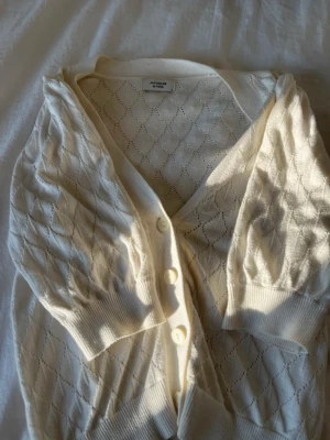 Vit kofta från Jacqueline de Yong - Snygg vit kofta från Jacqueline de Yong med knappar framtill och ett diskret hålmönster i diamantform. Står ingen storlek men skulle säga S 