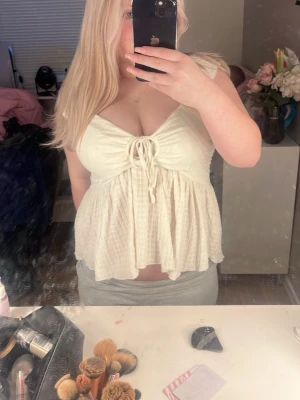 Vit linnetopp med knyt fram - Söt vit linnetopp med knyt fram och v-ringning. Toppen har en luftig och flowy passform med lätt rynk under bysten. Ärmlös design och mjukt, strukturerat tyg som känns som bomull eller linne. 