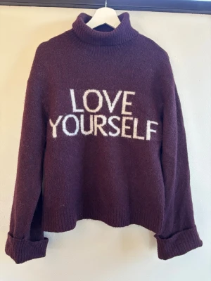 Vinröd med text Gina tricot 170 - Mysig vinröd stickad polotröja med vit text 'LOVE YOURSELF' framtill. Tröjan har långa ärmar med uppvikta muddar och är gjord i ett fluffigt, mjukt material och snyggt.
