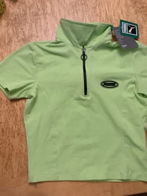 kortärmad tröja från Puma (croppad) - Sportig ljus neongrön topp från Puma med korta ärmar och hög krage. Toppen har en svart half zip-dragkedja framtill och Puma-logga på bröstet samt i nacken. Aldrig använt!