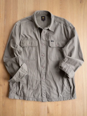 Khaki overshirt från Lee - Stilren khaki overshirt från Lee med relaxed fit. Skjortan har två bröstfickor med lock och knapp, klassisk krage och knäppning framtill. Tillverkad i ett slitstarkt bomullstyg som ger en avslappnad look. Perfekt att bära öppen över en t-shirt.