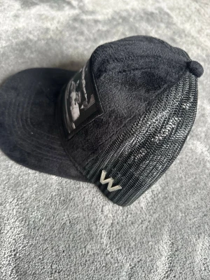 Svart keps med mesh och W-logga - Cool svart keps och en tydlig W-logga i metall på sidan. Framsidan har ett svartvitt motiv och kepsen har en klassisk böjd skärm. Materialet är en mix av tyg och mesh, perfekt för en avslappnad streetstyle.