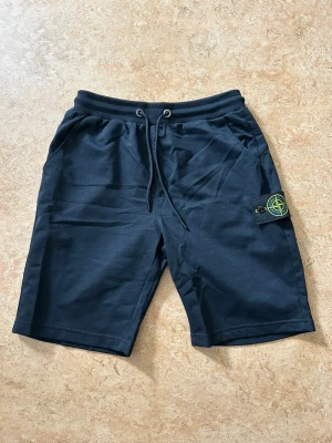 Svarta shorts från Stone Island - Säljer ett par marinblå shorts från Stone Island med klassisk logopatch på benet. Shortsen har snörning i midjan och två sidofickor. Helt nya Aldrig använda, liten i storlek. Min vikt är 67kg, längd 169cm och sitter lite för tajt för min smak. Kan skicka bild i chatten hur dom ser ut på 