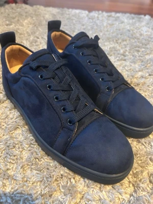 Marinblå  Christian Louboutin skor  - Snygga marinblå sneakers från Christian Louboutin i mocka med klassisk röd sula och svarta skosnören. Låg modell med diskret branding och lyxig känsla. Perfekta för dig som vill sticka ut med stilrena detaljer och exklusiv design. Helt nya prövat som en gång inomhus. Lägg bud på skorna om man vill. Om du vill ha mer bilder är de bara och fråga. Kan förhandla lite också.