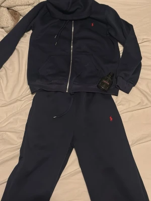 Mörkblå mjukisbyxor från Polo Ralph Lauren - Mörkblå mjukisbyxor från Polo Ralph Lauren med klassisk röd logga på benet. Byxorna har dragsko i midjan. Perfekt för chill dagar och avslappnade outfits.