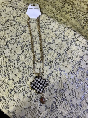 Guldigt lång halsband med rutigt hänge - Unikt halsband med dubbel guldfärgad kedja och fyrklöverformat hänge i svartvitt rutmönster. Hänget är dekorerat med glittriga stenar och en liten pärldetalj undertill. Perfekt för dig som gillar statement-smycken och vill sticka ut. 