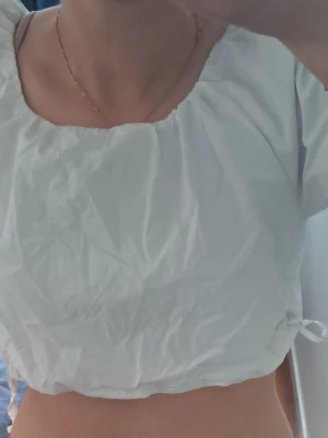 Vit croppad blus med puffärm - Säljer en vit croppad blus med puffärmar från Zara. Toppen har snörning i sidorna för justerbar passform och är tillverkad i ett tunt bomullsliknande material. Perfekt för en trendig och luftig look.