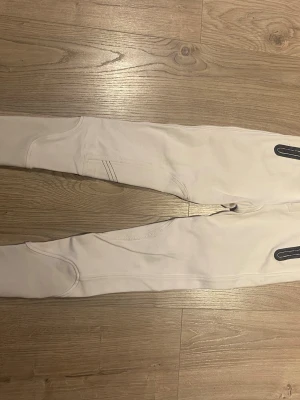 Vita leggings med detaljer - Säljer ett par vita leggings med snygga sömdetaljer och svarta dekorativa inslag på benen. De är figurnära och har en modern design som passar perfekt till en avslappnad look. Materialet är stretchigt och bekvämt.
