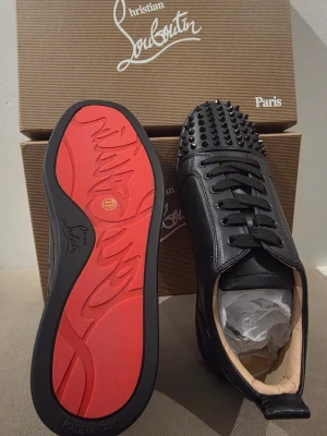 Svarta sneakers med nitar – Helt nya (Strl 41) - Säljer helt nya och oanvända svarta sneakers med nitar och röd sula i storlek 41. Modellerna är i samma stil men finns i två olika material. Totalt finns det tre par till salu.