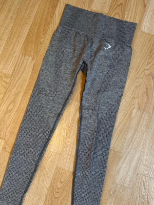 Grå seamless leggings från Gymshark - Säljer ett par grå seamless leggings från Gymshark med hög midja och diskret mönster längs benen. Stretchigt material som sitter skönt och följer kroppen. Perfekta för träning eller chill dagar. Gymshark-logga på höften. Använd 4 gånger 