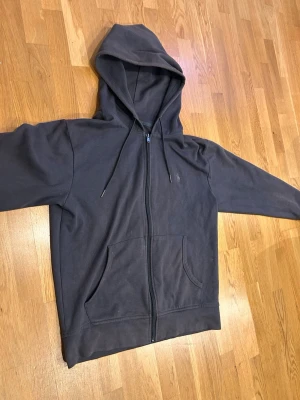 Mörkgrå hoodie från Polo Ralph Lauren - Säljer en mörkgrå hoodie med dragkedja från Polo Ralph Lauren. Hoodien har en klassisk huva med snören, två stora fickor framtill och diskret logga på bröstet. Perfekt för dig som gillar en enkel och stilren look.
