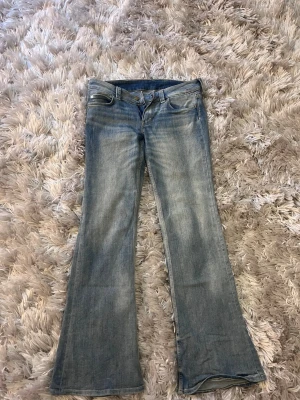 Bootcut jeans från Booty Bei - Snygga bootcut jeans från Booty Bei i ljusblå denim. Klassisk femficksmodell med låg midja och utsvängda ben. Materialet är 67% bomull, 32% polyester och 1% elastan för en bekväm stretch. Perfekta för en avslappnad och trendig look.