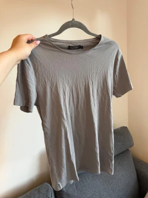 Grå basic t-shirt från dressman - En enkel grå t-shirt från dressman i mjuk bomull. Klassisk rund halsringning och korta ärmar. Perfekt till jeans eller shorts för en clean och avslappnad stil.