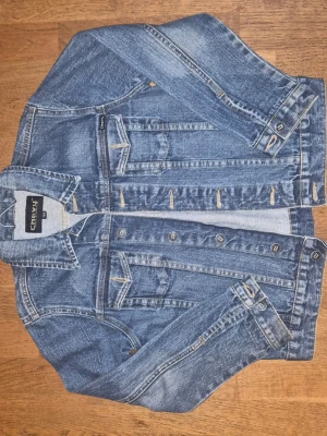 Blå jeansjacka från Chevy - Snygg blå jeansjacka från Chevy med klassisk design och coola detaljer som bröstfickor med lock och knappar framtill. Jackan har kontrastsömmar och är tillverkad i slitstarkt denim-material. Perfekt för dig som gillar streetstyle och denim.