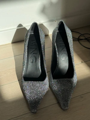 Glittriga silvriga klackar - Säljer ett par snygga pumps i silver med glittereffekt och spetsig tå. Skorna har en smal klack och är perfekta för dig som vill sticka ut. Materialet är täckt av glittrande yta och insidan är svart. Riktigt trendiga och ger en cool look till outfiten.