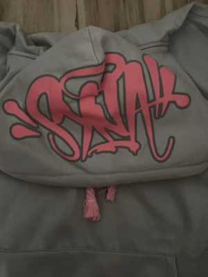 Syna world hoodie - Grå syna world hoodie med rosa märke och snören. Finns även byxor till! Ifall du vill köpa båda tillsammans så kan jag lösa det billigare!