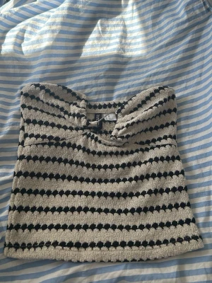 Tubtopp  - Säljer en somrig tubtopp från Divided i svart och beige. Toppen har en fin silver detalj framtil. Materialet känns mjukt och stretchigt, perfekt för varma dagar. Helt oanvänd!🥰storlek xs men är mer som en xxs! Den har även som silikon remsor över bysten så den hålls uppe!