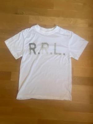 Vit RRL t-shirt med tryck - Säljer en vit t-shirt från RRL med stort tryck på bröstet. Klassisk passform med rund hals och korta ärmar. Perfekt till jeans eller shorts för en enkel och clean look.
