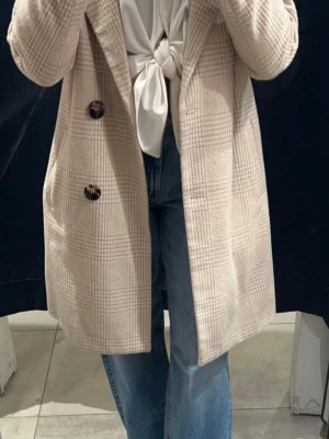 Beige rutig kappa med knappar - En superfin beige kappa med rutigt mönster. Kappan är fodrad. 