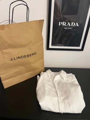 Vit linneskjorta från J.Lindeberg - Klassisk vit skjorta från J.Lindeberg i svalt linne. Skjortan har lång ärm, knappar framtill och en tidlös krage. Perfekt för en clean och stilren look.