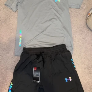 Grå t-shirt från Under Armour - OBS: bara t shirt.Snygg grå t-shirt från Under Armour med färgglad logga på bröstet och text längs sidan. T-shirten är kortärmad och har en klassisk passform, perfekt för dig som gillar sportig och stilren look.