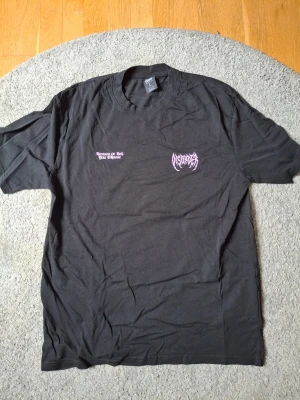 Svart band-tshirt från Sound, L - Svart t-shirt från Sound med relaxed fit och tryck i lila på bröstet. Klassisk rund halsringning och korta ärmar. Perfekt för dig som gillar bandtröjor och vill ha en avslappnad stil.