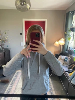 Grå hoodie med huva och snören - Säljer en enkel och stilren grå hoodie med huva och vita dragsnören. Hoodien har en klassisk passform och är tillverkad i mjukt material, perfekt för en avslappnad look. Inga synliga loggor eller tryck, passar till det mesta.