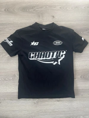 Svart Chaotic t-shirt från FSBN - Säljer en svart t-shirt från FSBN med relaxed fit och trycket 'CHAOTIC' i vitt framtill. T-shirten har coola vita loggor på bröstet och ärmarna, perfekt för en streetwear-look. Tillverkad i mjuk bomull för skön känsla hela dagen. Helt ny oanvänd
