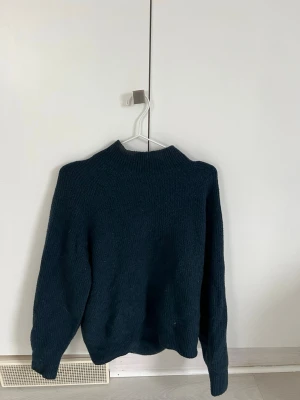 Mörkblå stickad tröja från Uniqlo - Mysig mörkblå stickad tröja från Uniqlo med hög hals och långa ärmar. Tröjan har en enkel, klassisk design och är tillverkad i ett mjukt material som passar perfekt för kyliga dagar.