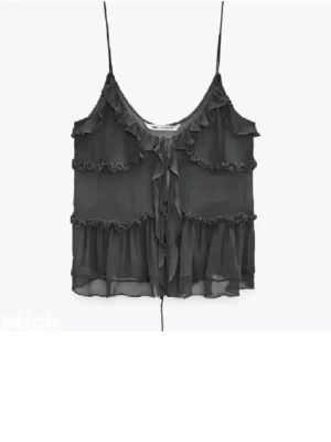 Svart volangprydd topp med tunna band - Snygg svart topp med tunna axelband och volangdetaljer i flera lager. Tillverkad i ett lätt, transparent tyg. Knytband framtill för extra detalj.