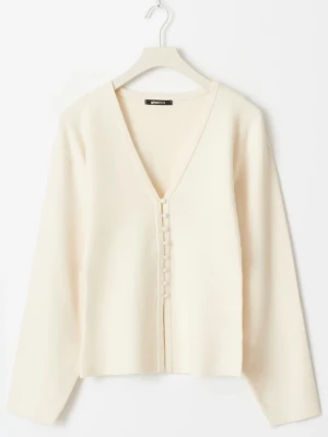 Krämvit kofta med knappar - Helt ny med prislapp kvar. Säljer en stilren krämvit kofta från Gina med djup V-ringning och dekorativa tygklädda knappar framtill. Koftan har lång ärm och rak passform, perfekt för lager på lager. Materialet känns mjukt och lätt.