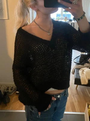 Svart virkad stickad tröja - Säljer en svart, virkad stickad tröja med v-ringning och avslappnad passform. Tröjan har långa ärmar och bred mudd vid ärmslut och nederkant. Perfekt att bära över ett linne eller topp för en cool lager-på-lager-look.