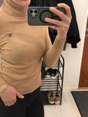 Beige polotröja från Gant 100% får ull - Säljer en beige stickad polotröja från Gant med diskret blå logga på bröstet. Tröjan har lång ärm, ribbade muddar och är i mjukt material. 100% får ull 