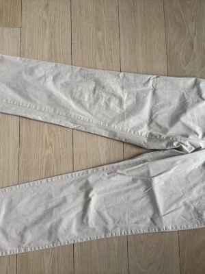 J.Lindeberg - Ljusbeige chinos med rak passform - Säljer ett par ljusbeige chinos med rak passform. Byxorna har klassisk design utan synliga detaljer eller loggor och är tillverkade i ett mjukt bomullstyg som känns skönt mot huden. Perfekta för dig som gillar en clean och enkel stil.