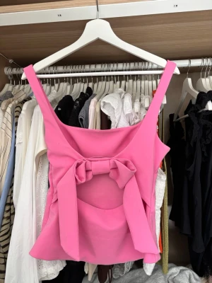 Rosa linnetopp med rosett och cut-out från Zara - Snygg rosa topp med breda axelband och figurnära passform. Toppen har en stor rosett och cut-out detalj i ryggen som ger en unik look. Perfekt att styla med jeans eller kjol för en trendig outfit💕Använd fåtal gånger och i bra skick! 