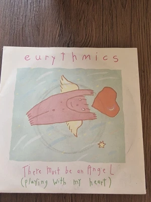 Eurythmics vinylsingelää - Säljer en vinylsingel med Eurythmics – 'There Must Be an Angel (Playing With My Heart)'. Omslaget har ett tecknat motiv med en rosa ängel och hjärta på ljus bakgrund. Baksidan har låtinfo och RCA-logga. Perfekt för samlare av 80-talsmusik.