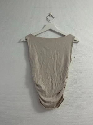 Beige ärmlös linne - Säljer ett enkelt och stilren beige linne utan ärmar. Linnet har rund halsringning och är tillverkad i ett mjukt, stretchigt material som sitter skönt mot kroppen. Perfekt att styla med jeans eller kjol för en clean look.