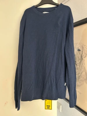 Mörkblå stickad tröja Jack & Jones - Mörkblå stickad tröja från Jack & Jones med rund halsringning och ribbade muddar vid ärmslut och nederkant. Enkel och stilren design som passar till många olika outfits. Tillverkad i mjukt material för skön känsla.