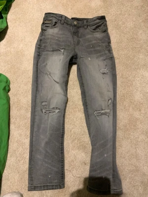 Grå Supply & Demand slitna jeans med hål  - Säljer ett par grå jeans från Supply & Demand med slitningar och hål på både lår och knän. Jeansen har en klassisk femficksmodell och raka ben. Perfekta för dig som gillar en avslappnad och trendig streetstil. Orginalpris 420kr.