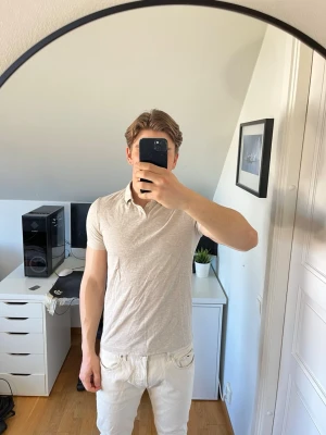 Beige pikétröja från Bläck - Snygg beige pikétröja från Bläck med klassisk krage och korta ärmar. Tillverkad i mjukt bomullsmaterial som känns skönt mot huden. Hör gärna av dig vid frågor!