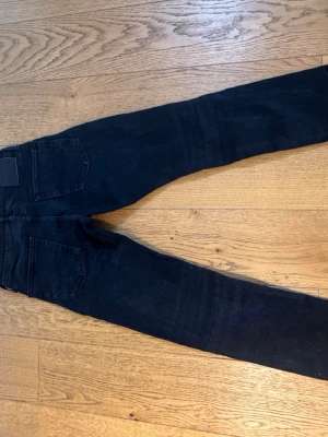Svarta slim fit jeans - Säljer ett par svarta slim fit jeans med klassisk femficksdesign och raka ben. Jeansen har knapp och dragkedja framtill samt diskret lapp på bakfickan. Perfekta för dig som gillar en enkel och stilren look. De är i storlek 30W 34L, de passar som 31W 32L ish 