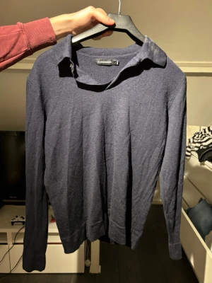 Mörkblå tröja med krage från Lindbergh - Snygg mörkblå tröja från Lindbergh med klassisk krage och lång ärm. Tillverkad i ett tunt, mjukt material som passar perfekt för lager på lager. Enkel och stilren design som funkar till det mesta.