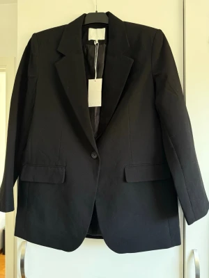 Svart oversized kavaj från NA-KD - Stilren svart oversized kavaj från NA-KD med klassisk krage och enkel knappstängning. Helt ny med prislappen kvar.